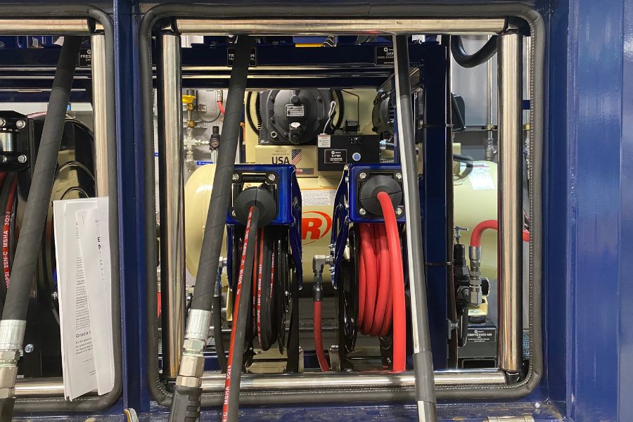 Hose reels behind a stainless guard on a lube island dispense bay, with room on the rack for a further dispense point